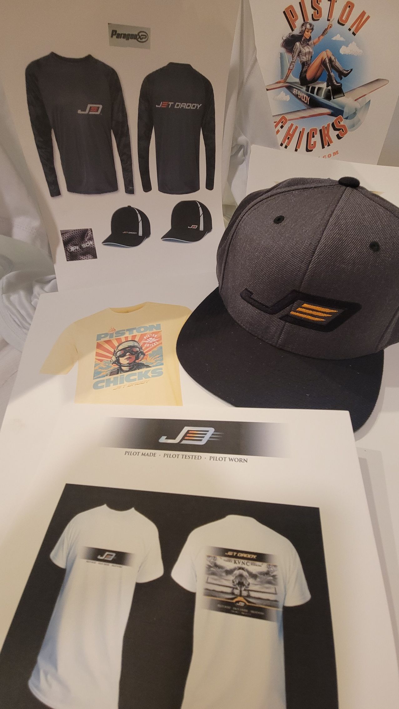 Merchandise display featuring gray and black hats, long-sleeved shirts, and t-shirts with a logo.