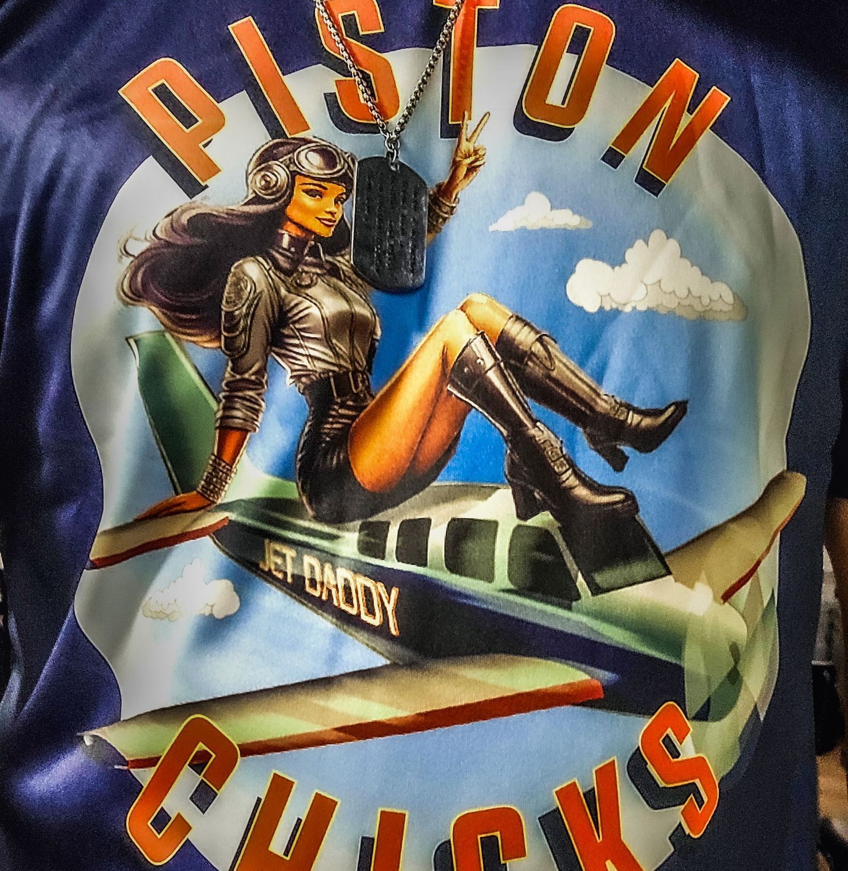 Navy blue shirt with a retro-style graphic of a woman in a pilot outfit, lounging on a plane, text