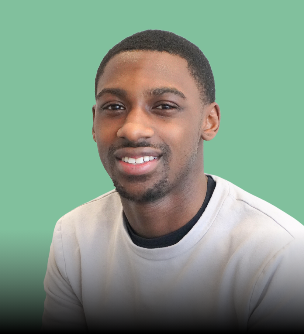 A young man with a beard is smiling for the camera while wearing a white sweater.