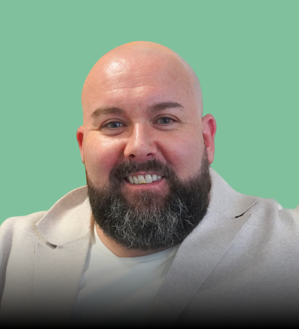 A bald man with a beard is wearing a white jacket and smiling.