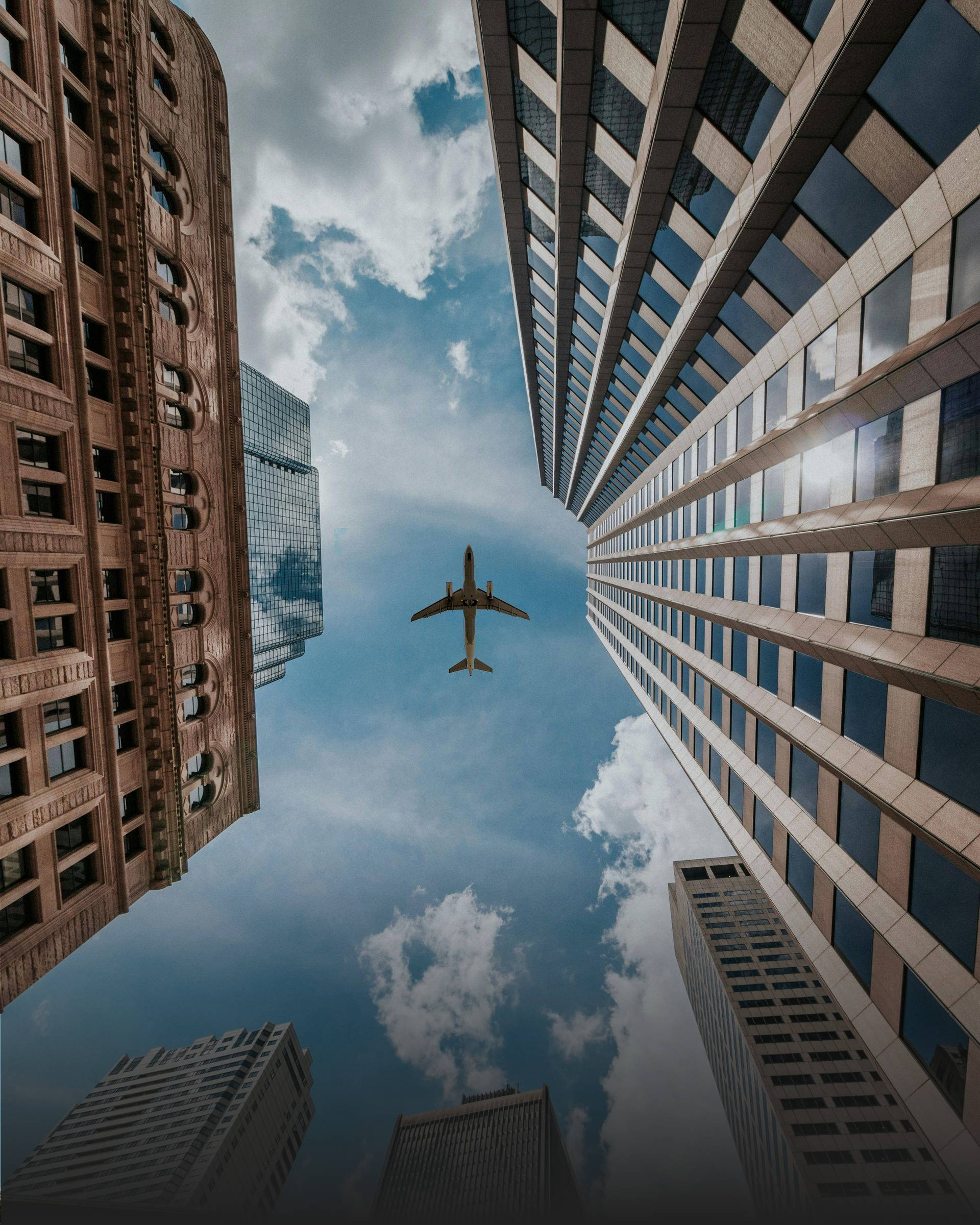 A plane is flying through the air between two tall buildings.