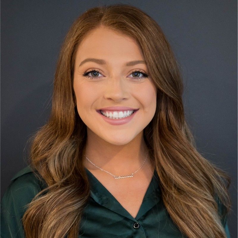 A woman wearing a green shirt and a necklace is smiling for the camera.