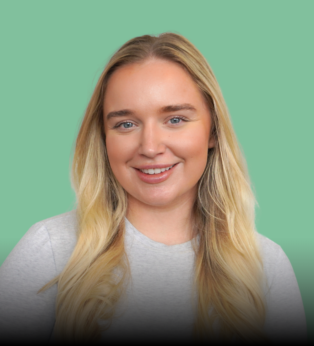 Blonde woman with a slight smile, light grey sweater, against a light green background.