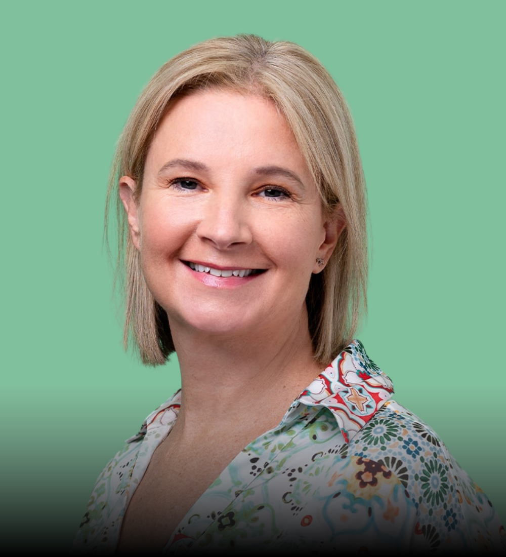 A woman is smiling and wearing a floral shirt on a green background.
