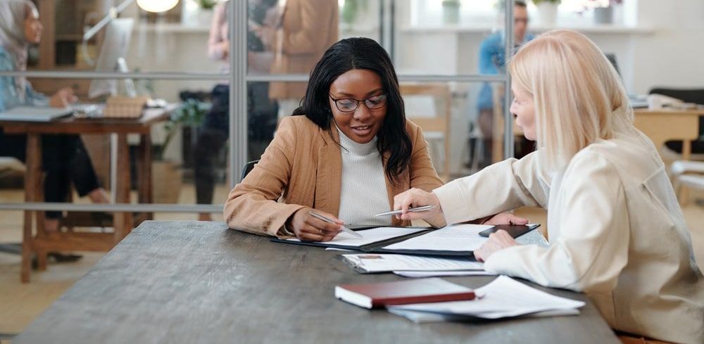 Two women are sitting at a table looking at papers.