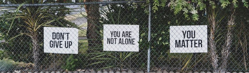 Three signs on a chain link fence saying