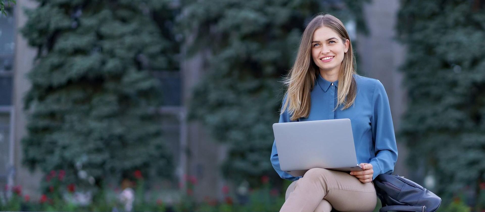 A woman is sitting on a bench holding a laptop computer.