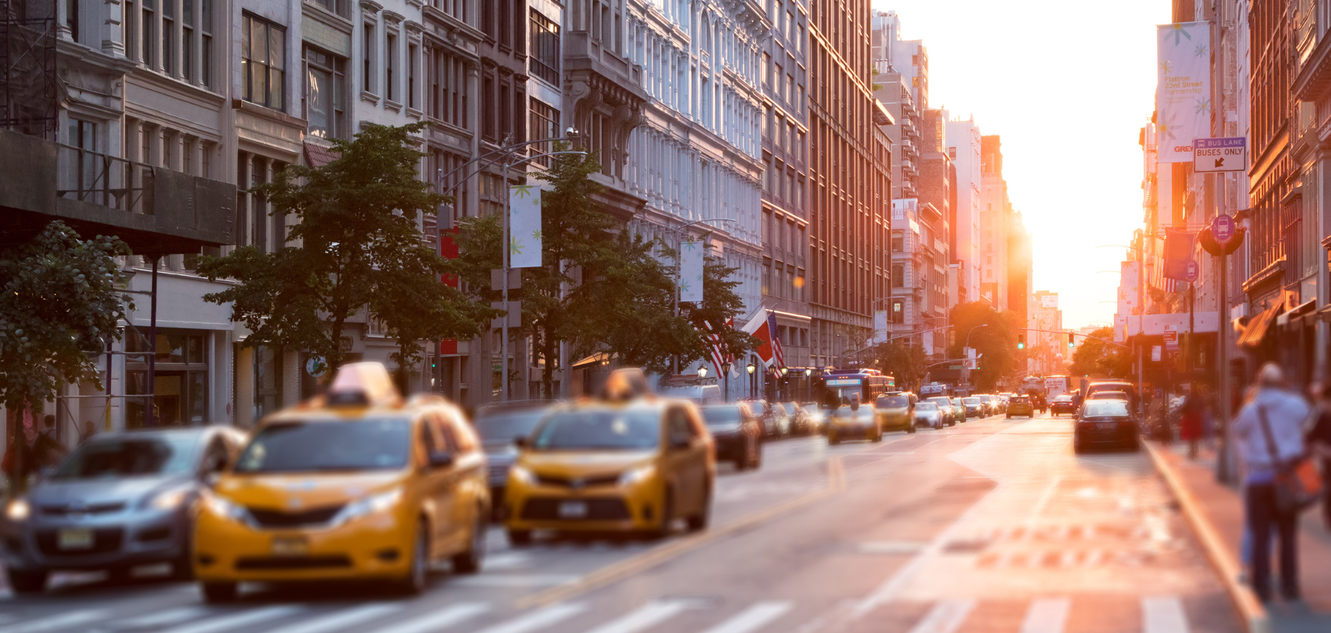 A row of yellow taxis are driving down a city street at sunset.