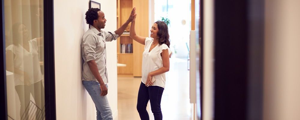 A man and a woman are giving each other a high five in a hallway.