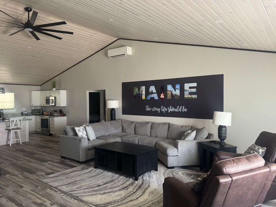Modern living room with gray sectional, brown recliner, black coffee table, and large “Maine” wall art.
