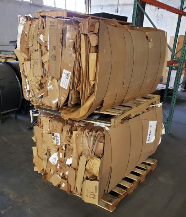 Two bales of flattened cardboard stacked on wooden pallets in a warehouse.