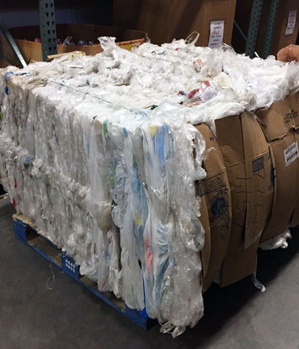 Bale of plastic bags stacked on a wooden pallet, enclosed in cardboard, inside a warehouse.