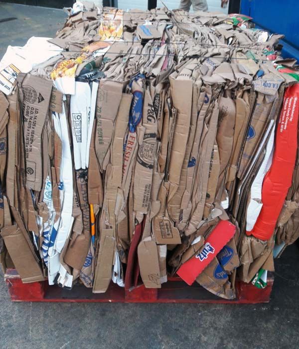 A compacted bale of cardboard, with red, blue, and brown hues, sits on a wooden pallet.