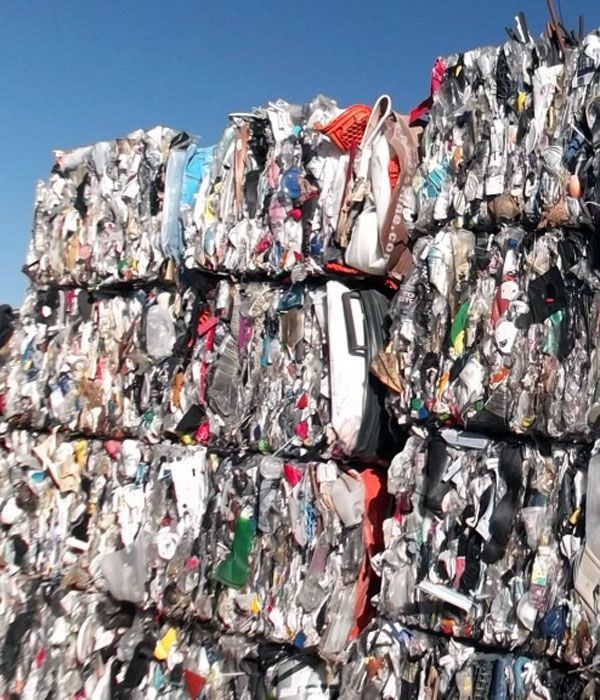 Pressed bales of shredded clothing, likely for recycling, outdoors under a blue sky.