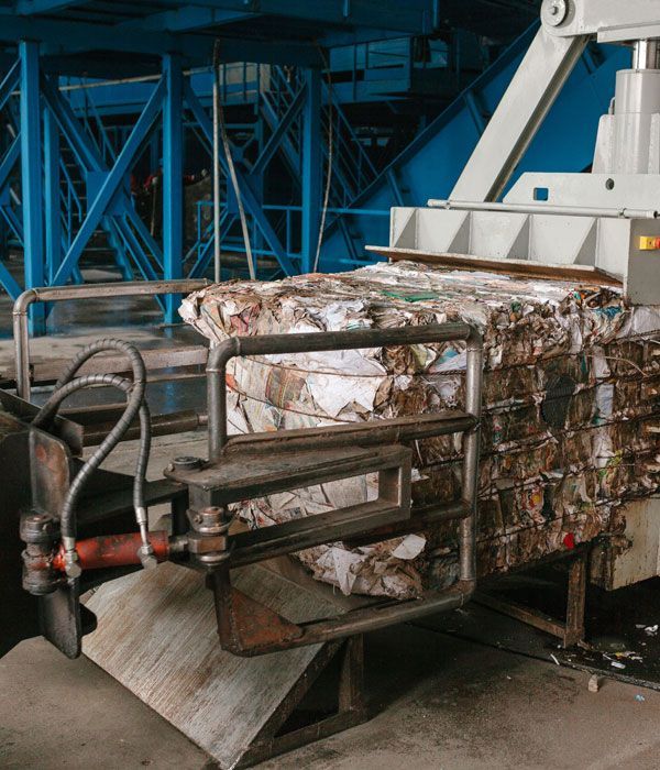 Bale of compressed paper held by a machine in an industrial setting, blue steel structure in the background.