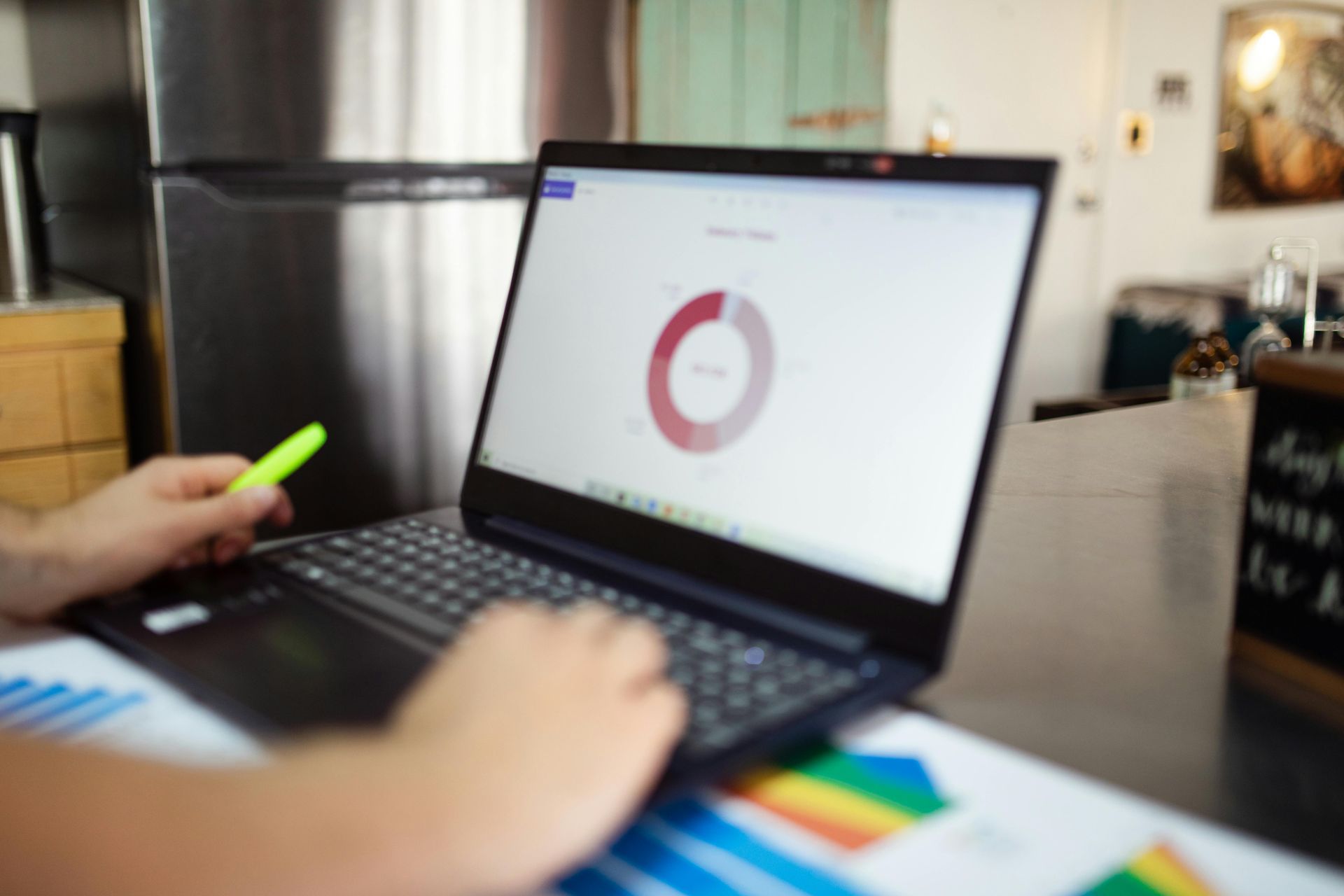 Person working on laptop with a pie chart. A highlighter and printed charts are on the desk.