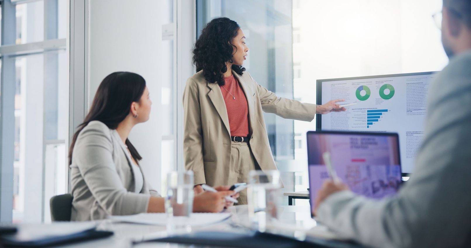 Businesswoman presenting financial data on screen to colleagues in an office.
