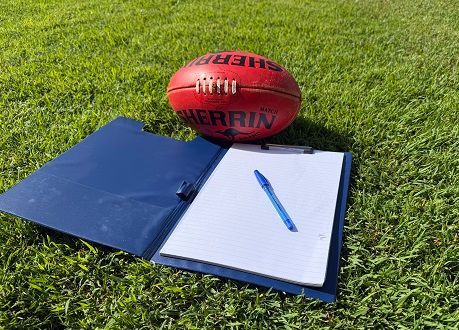 Blue binder, lined notebook, and pen on grass with a red football behind them.