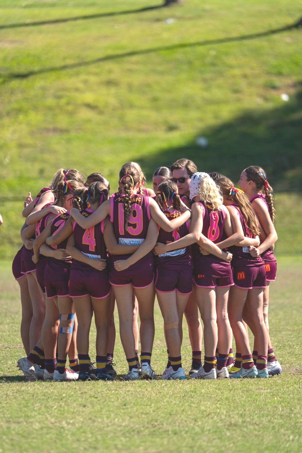 Maroon-clad sports team huddled together on a grassy field before a game