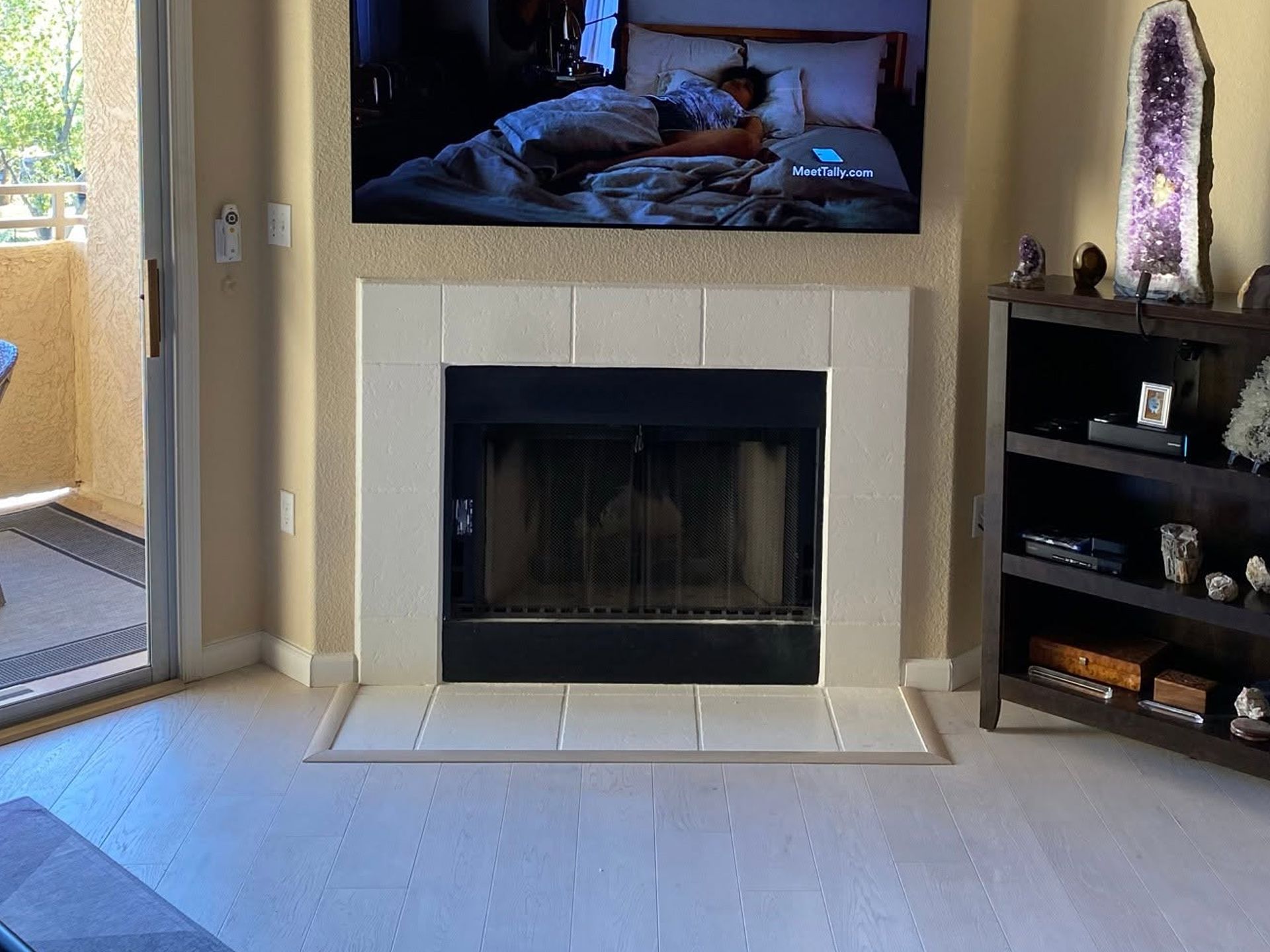 Living room with a wall-mounted TV above a fireplace and a small shelf beside it
