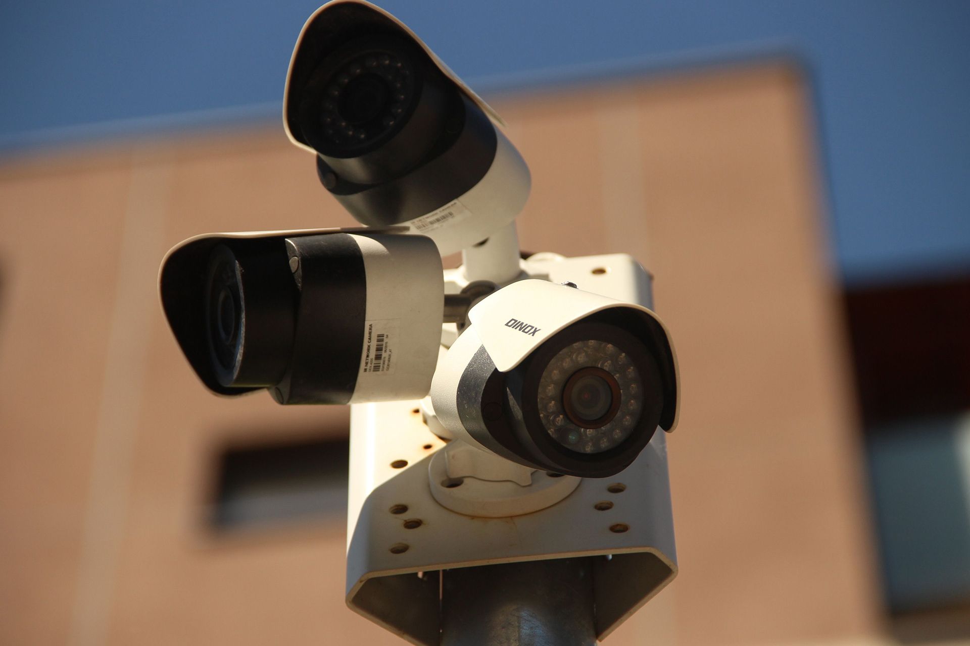 Three security cameras mounted on a pole against a blurred building backdrop