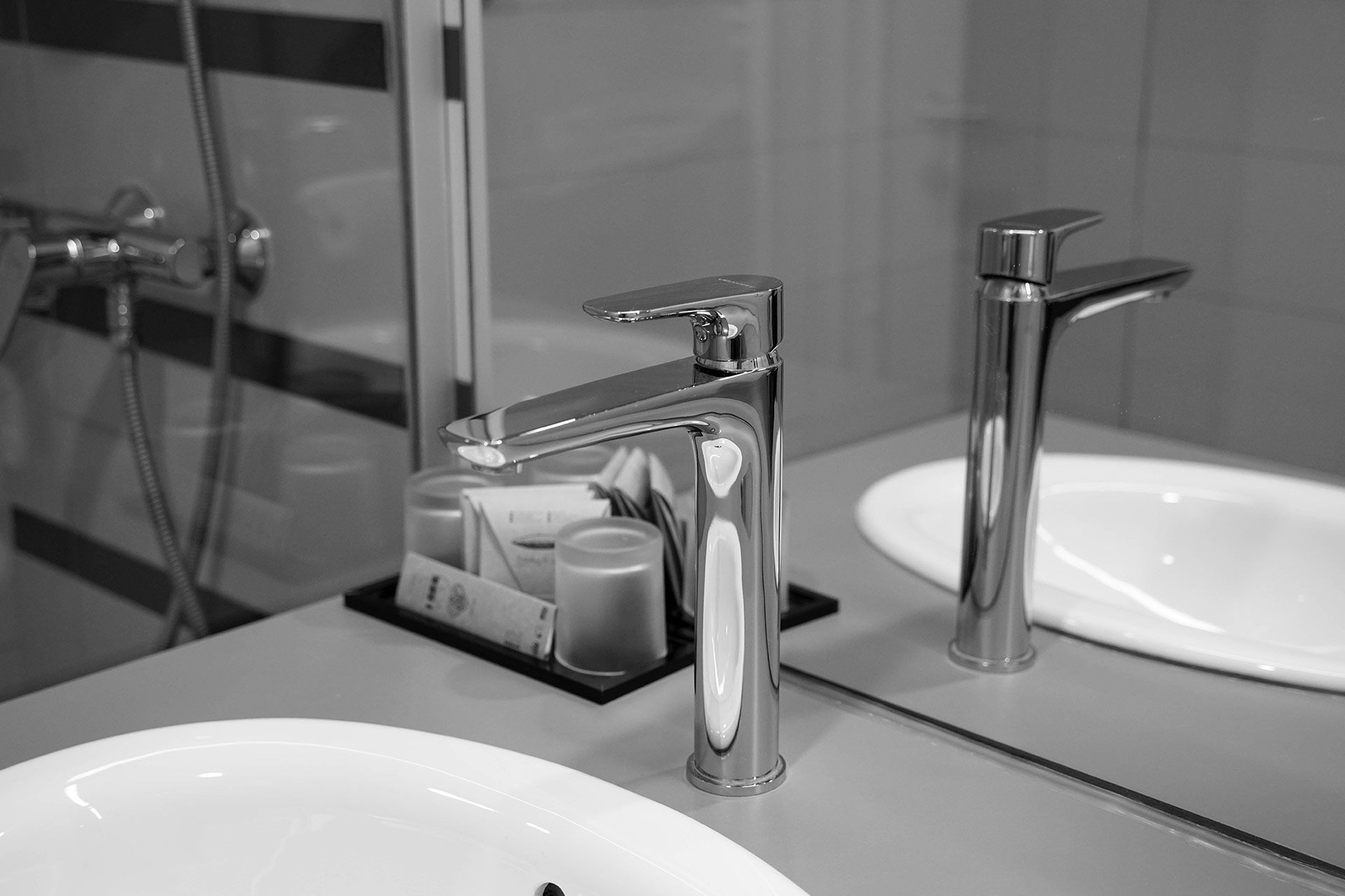Chrome bathroom faucet beside a sink and soap dispenser, reflected in a mirror.