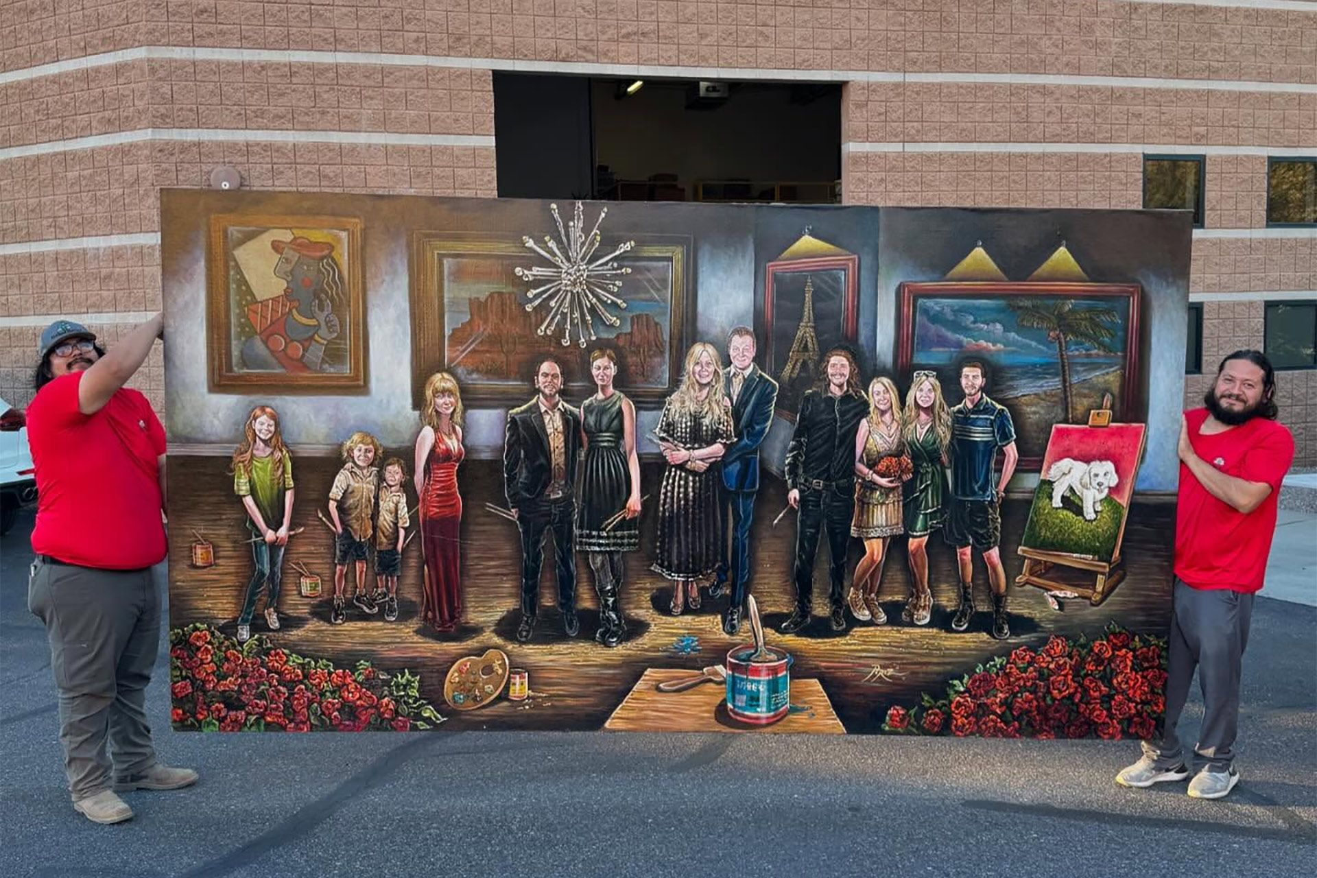 Group posing in front of a large mural on a brick wall, with two people in red shirts at the sides.