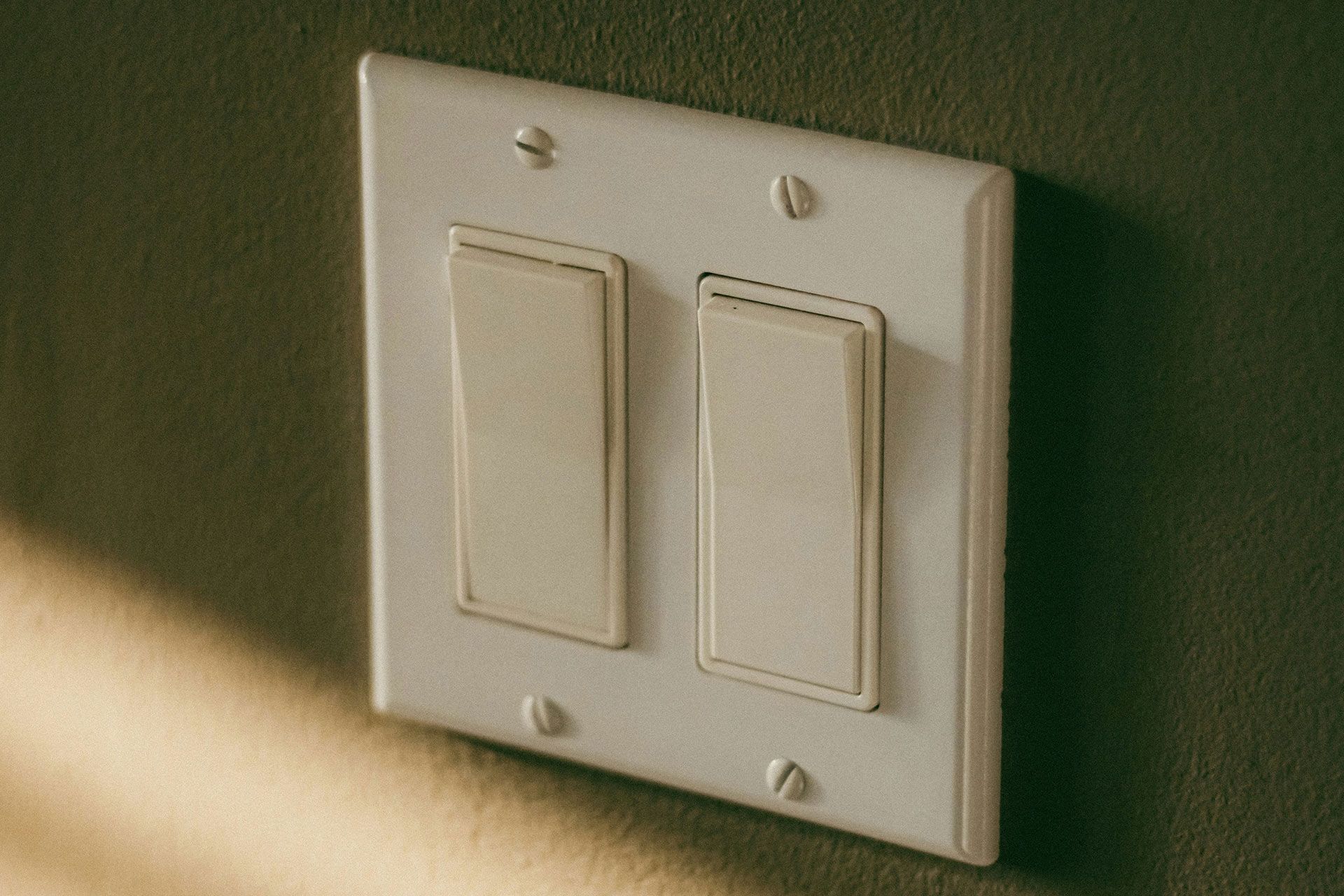 White dual light switch on a wall with warm sunlight and shadow.
