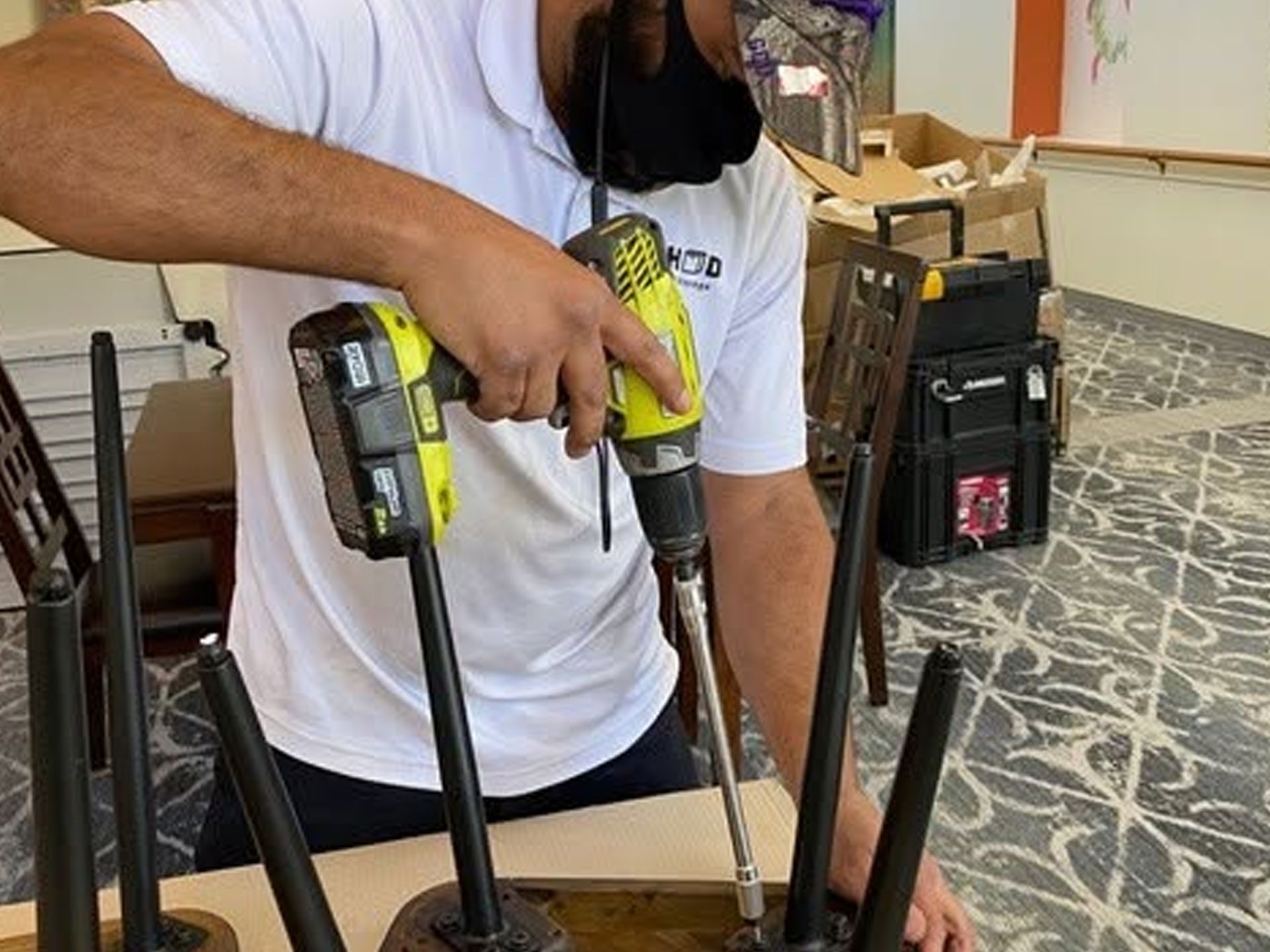 Person using a cordless drill to drive a screw into a wooden surface in a workshop.