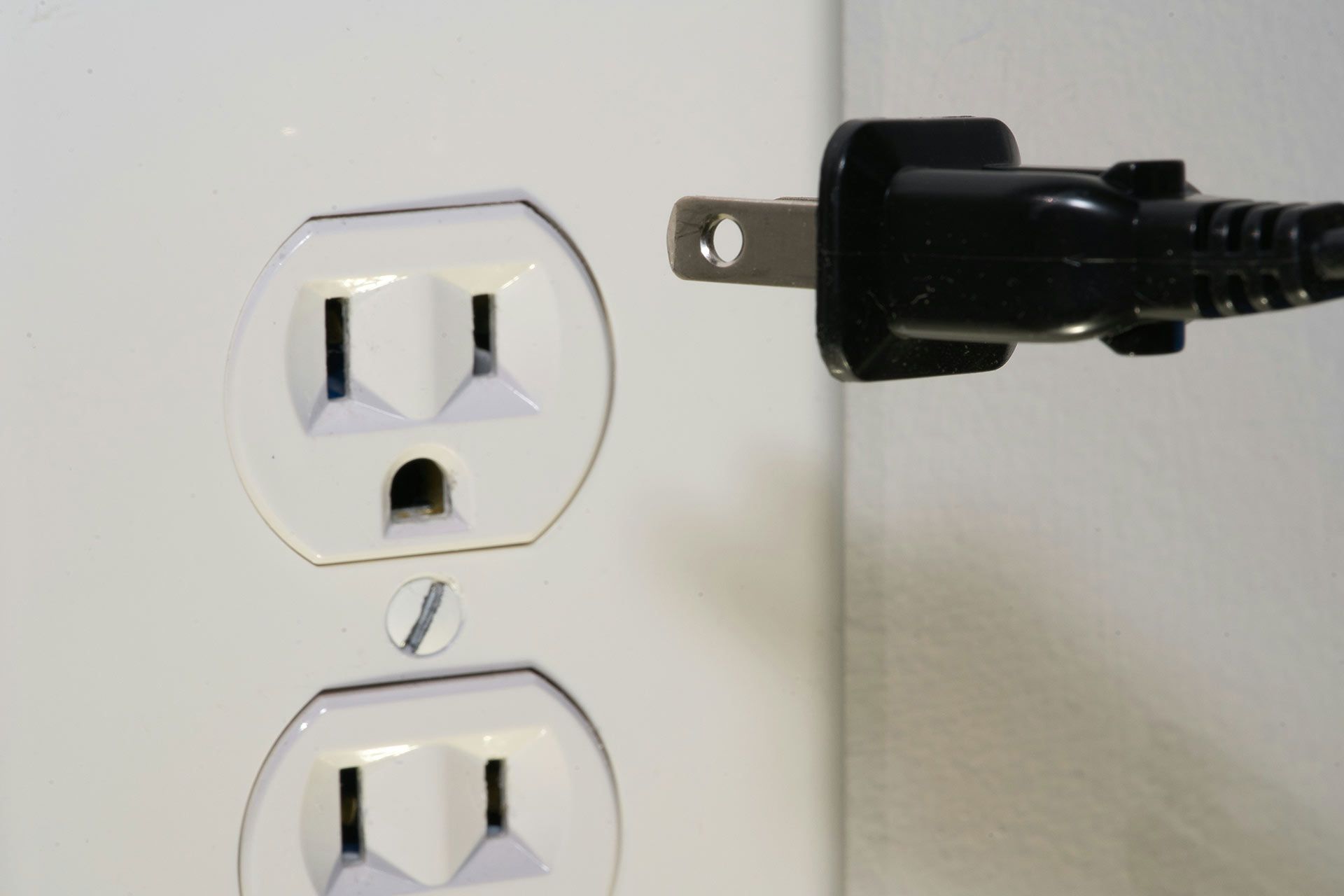 White wall outlet with a black plug inserted into the top socket.