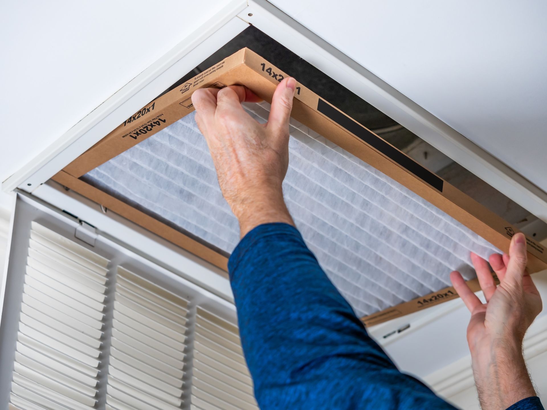Hands installing a ceiling air filter in a white HVAC vent frame