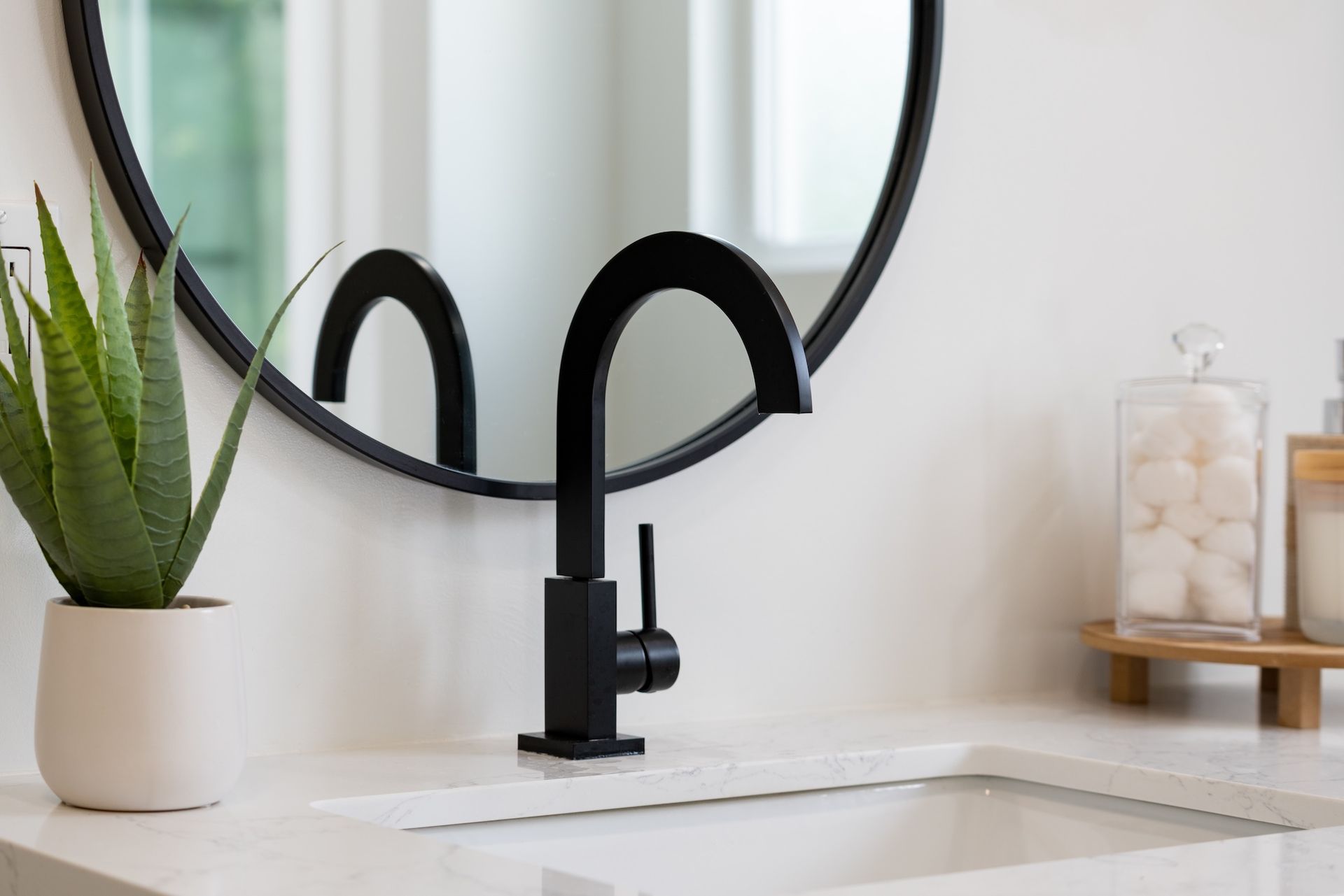 Modern bathroom sink with black faucet, round mirror, and potted plant on the counter