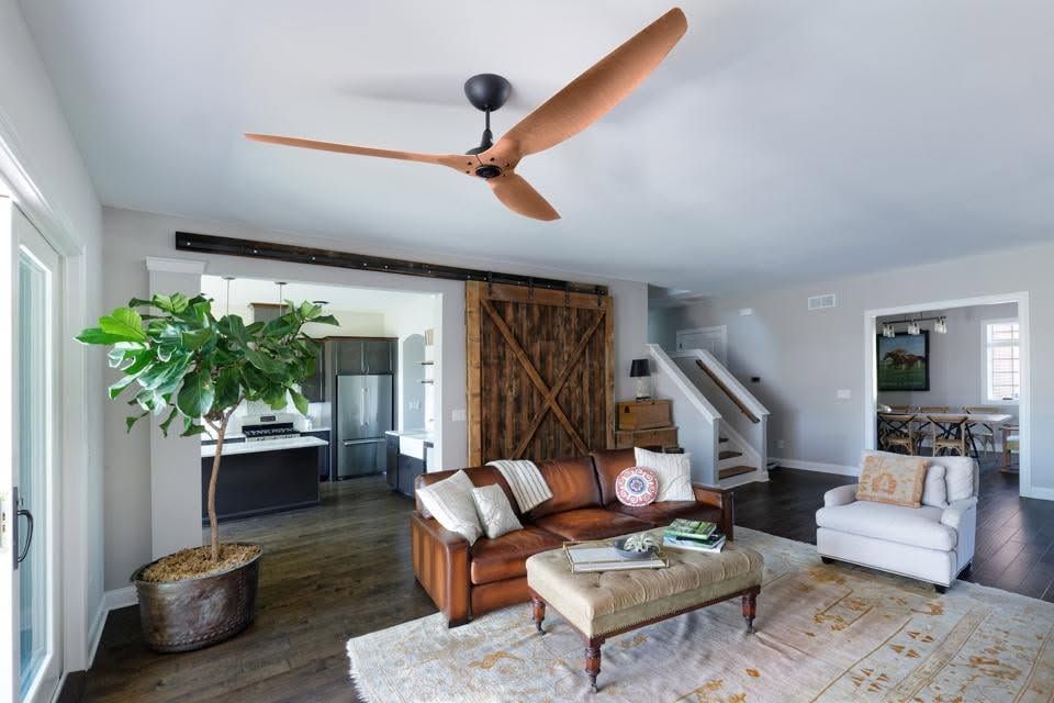 Modern living room with leather sofa, white armchair, ceiling fan, and rustic barn doors