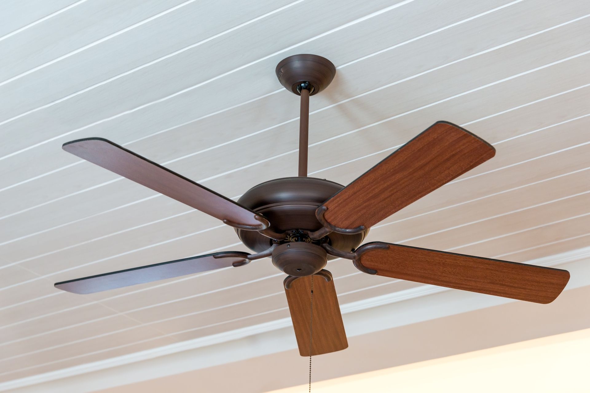 Dark ceiling fan with wooden blades on a white ceiling