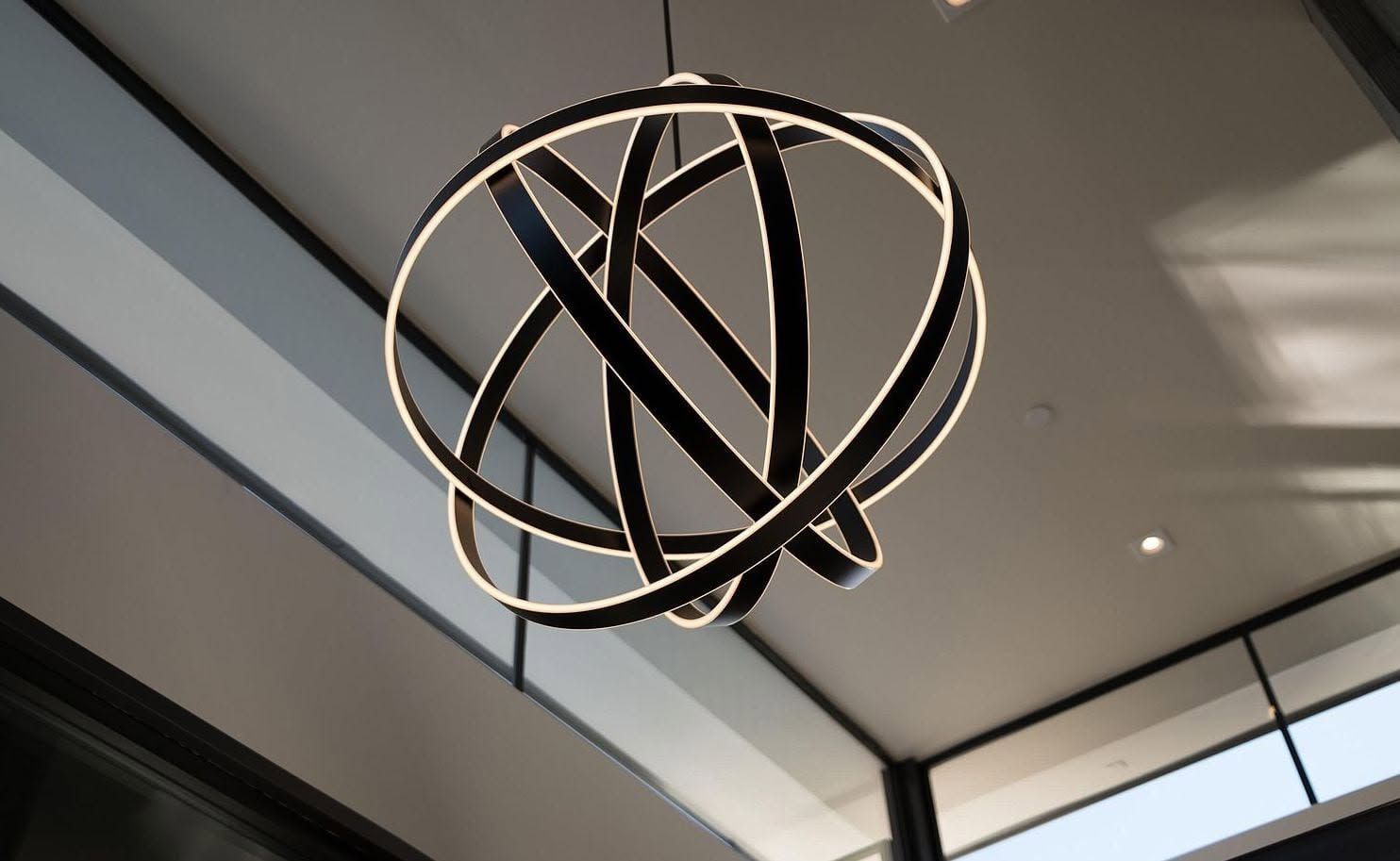 Abstract black metal sculpture with looping rings hanging from a ceiling in a modern interior.