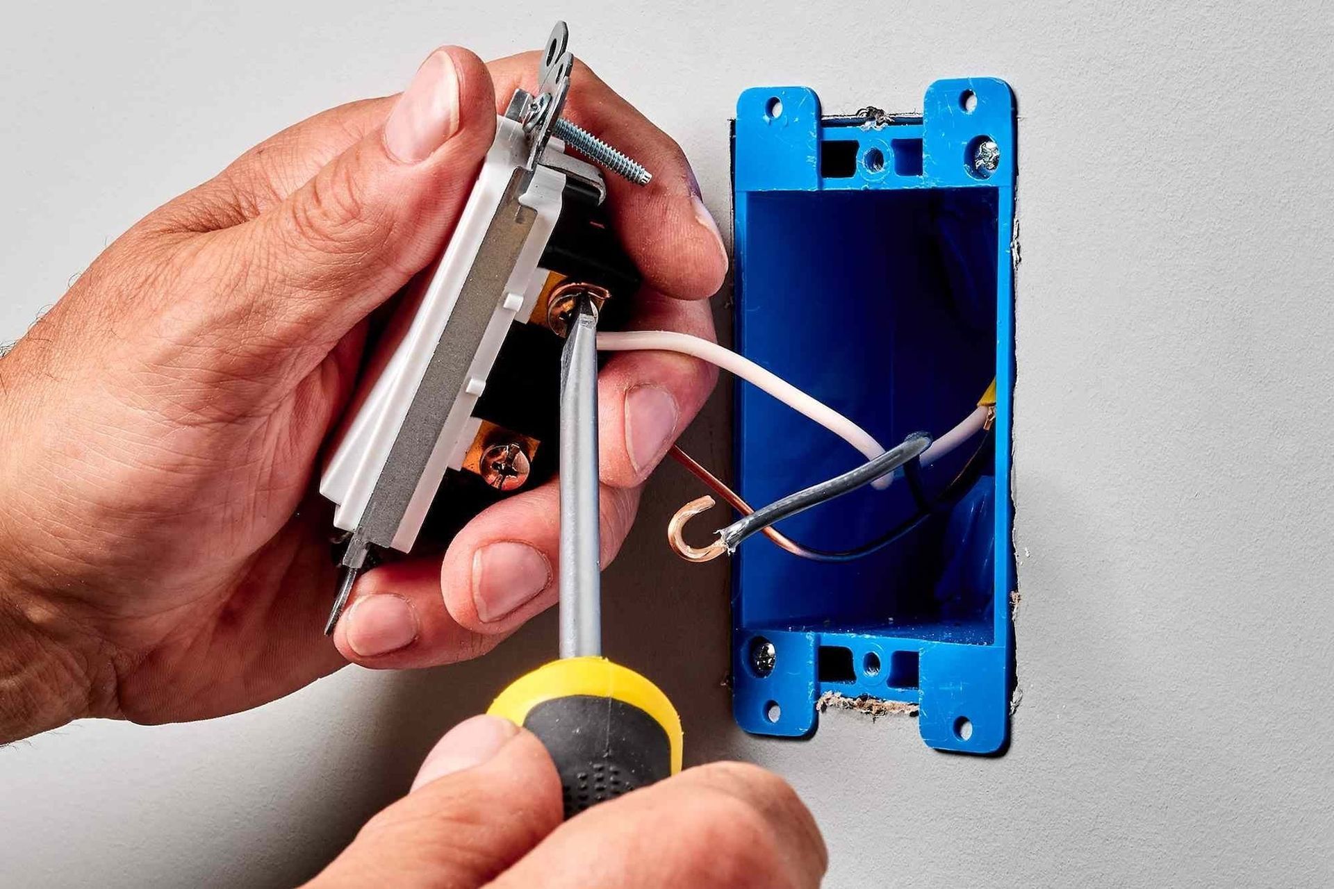 Hand wiring an electrical switch into a blue wall box with a screwdriver