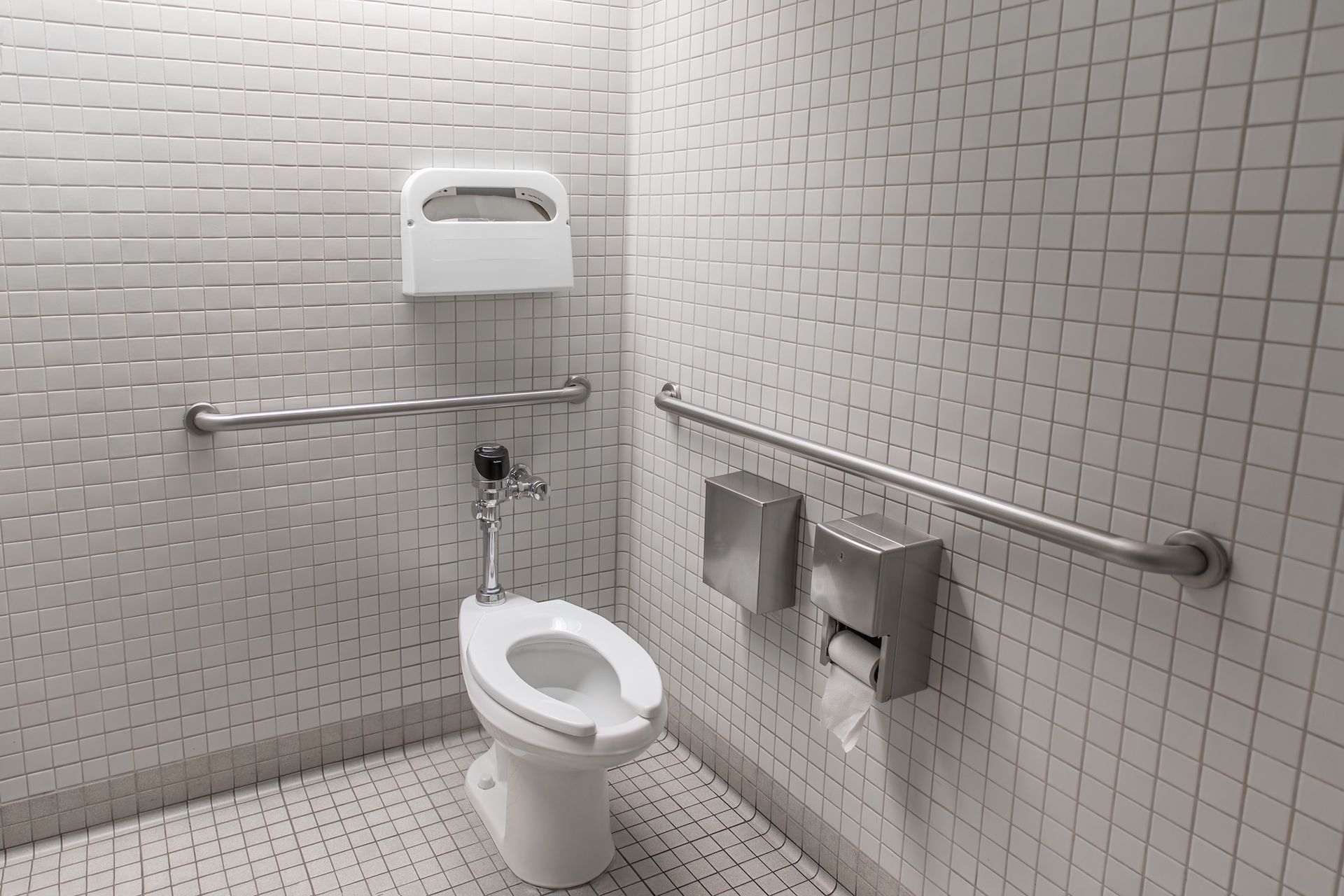 Accessible public restroom with toilet, grab bars, and wall-mounted dispensers.