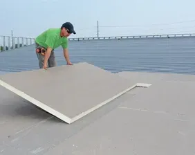A man is laying a large piece of plywood on top of a roof.
