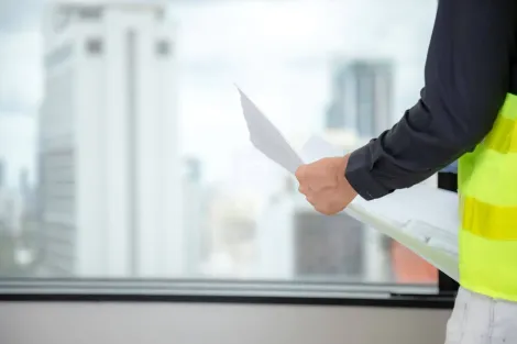 A man in a yellow vest is holding a piece of paper in front of a window.