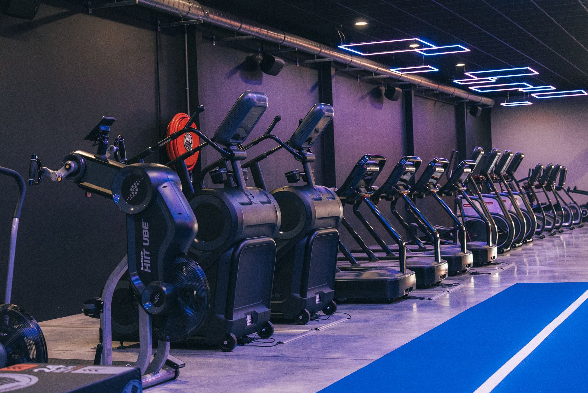 Een sportschool met veel fitnessapparatuur en een paars neonbord.