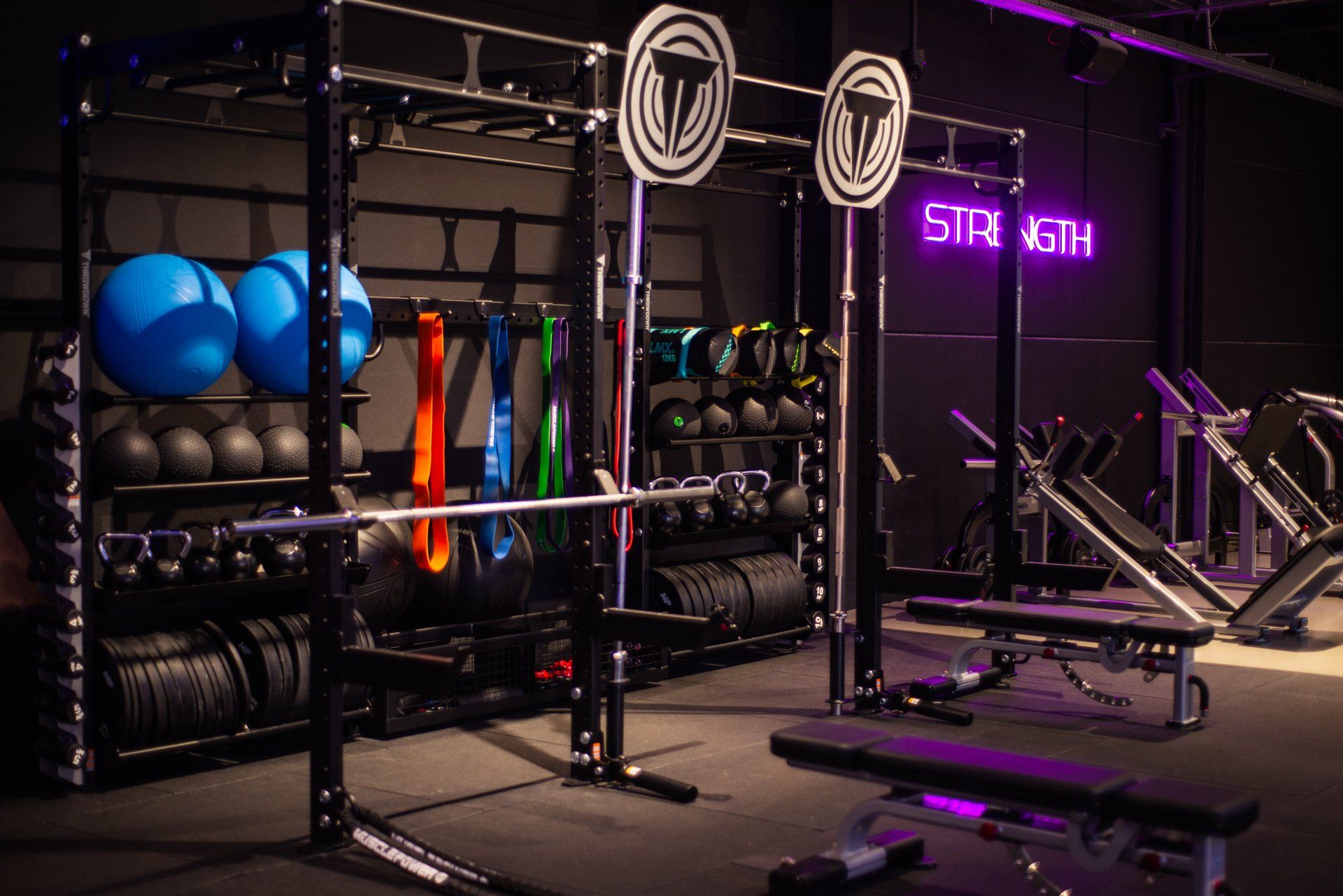 Een sportschool met veel fitnessapparatuur en een neonreclame met de tekst 'kracht'.