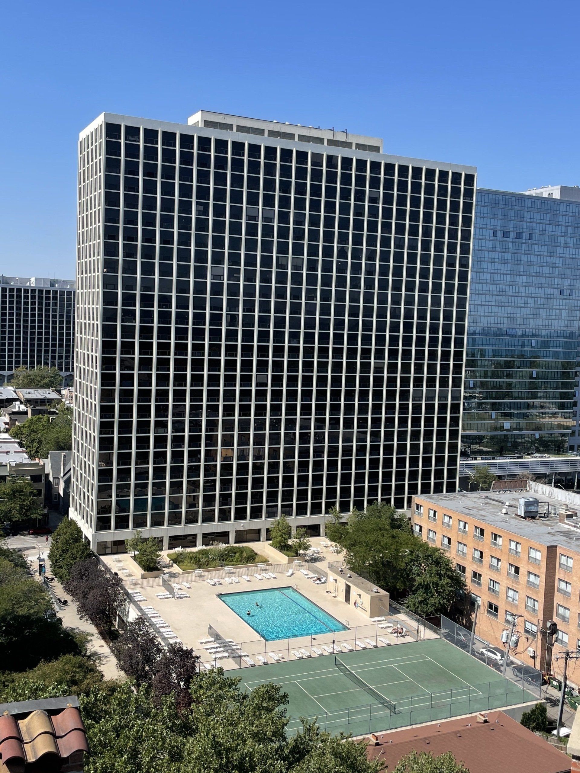 High-rise apartment building with many windows, pool, and tennis court on a sunny day.