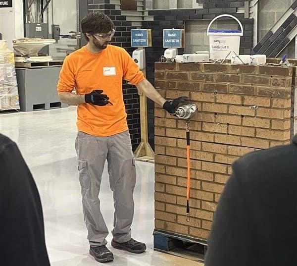 A man is standing in front of a brick wall demonstrating Masonry stabilization