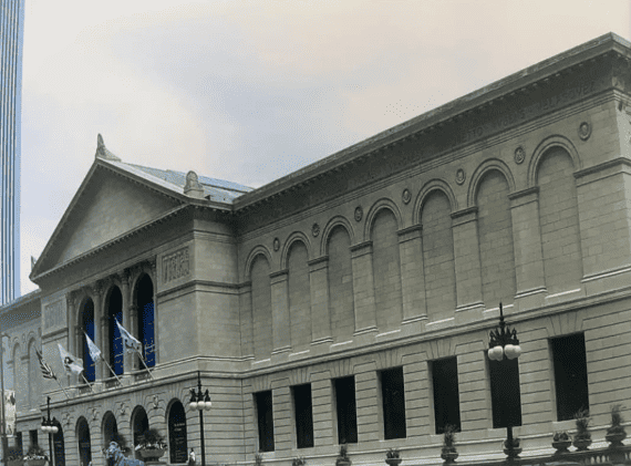 Large stone museum building with arched windows, columns, and flags outside under a cloudy sky