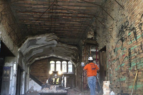 Interior of a dilapidated building under construction; a worker in safety gear stands near debris.