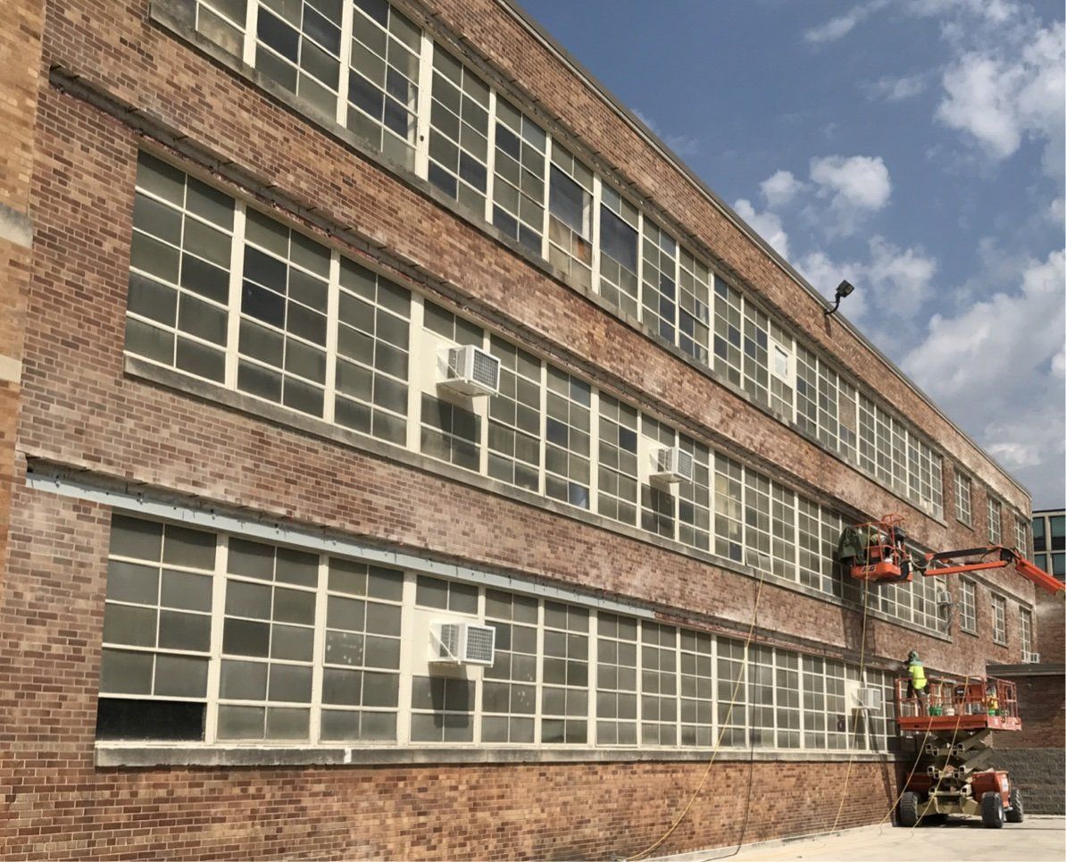 Brick building with many rectangular windows. Construction workers in lift. Sunny day.