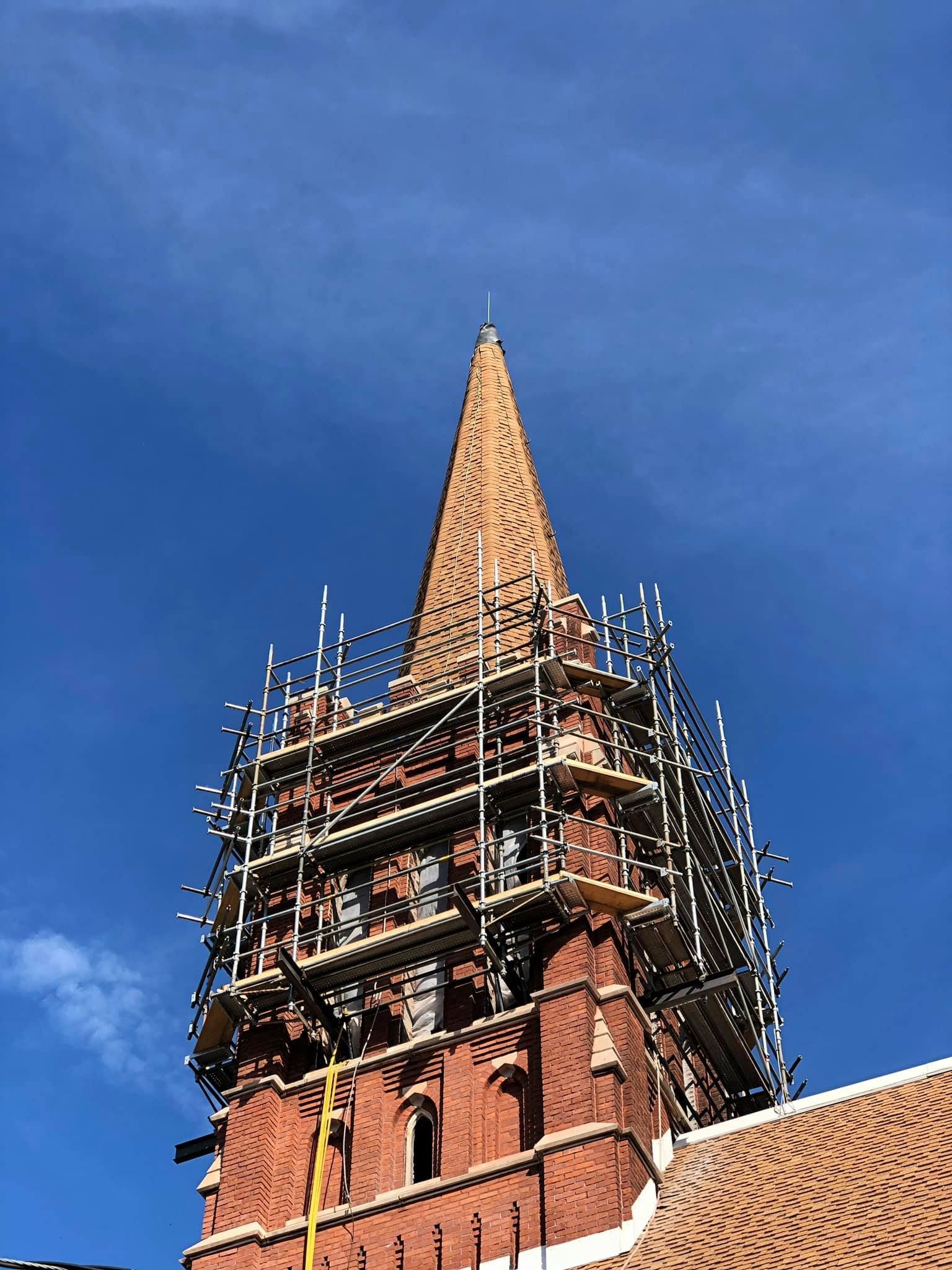 St. Joseph Church's brick steeple with scaffolding around it and a blue sky in the background.