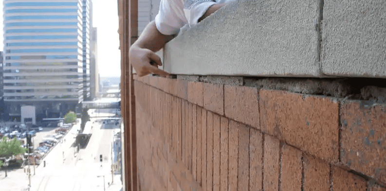 Person leaning on a brick ledge above a city street, with tall buildings in the background