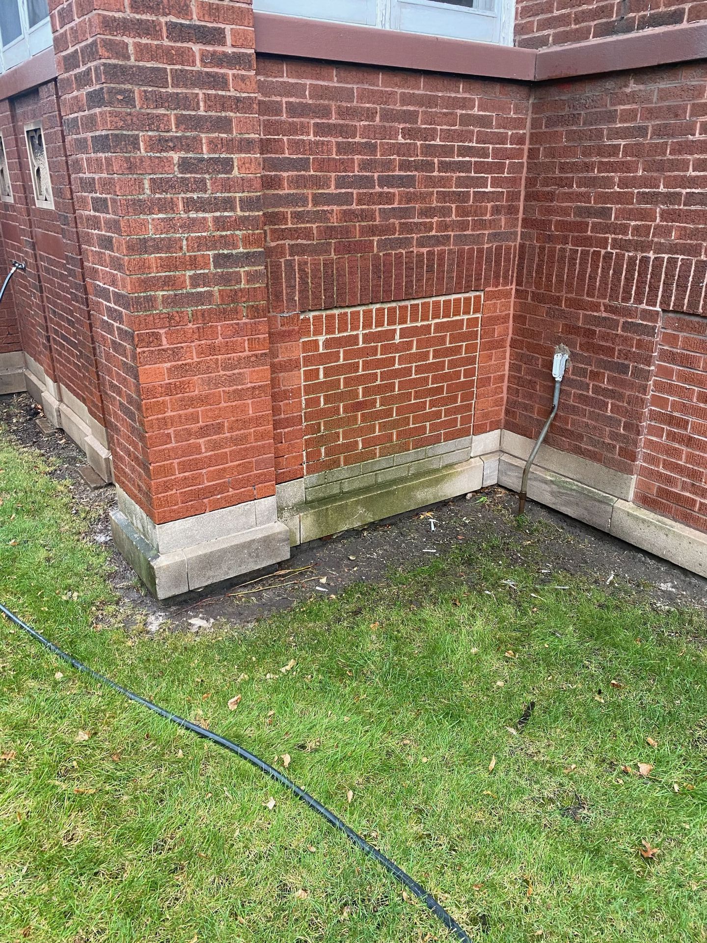 A masonry cleaning mock-up performed by RestoreWorks on a church rectory in Gary, Indiana. The image shows a section of a red brick wall where cleaning has been tested, revealing a noticeably brighter area compared to the surrounding weathered bricks. The lower portion of the wall has visible dirt and biological staining, highlighting the effectiveness of the restoration process. The mock-up helps determine the best cleaning method for the full masonry restoration project.