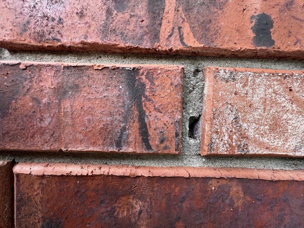 Close-up of a brick wall with red-brown bricks and gray mortar, showing some dark areas.